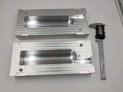 Deux blocs en aluminium avec des formes intérieures creusées, placés côte à côte, avec un pied à coulisse numérique à côté.