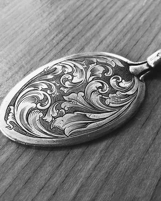 Médaillon en argent orné d'ornements floraux gravés, posé sur une surface en bois.