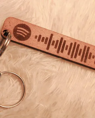 Porte-clés avec une étiquette en bois gravée d'un logo Spotify et d'un code QR, posé sur une surface en peluche beige