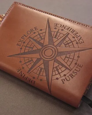 Une sacoche en cuir marron avec une boussole gravée portant les mots exploration, expérience, pursuit, détente.