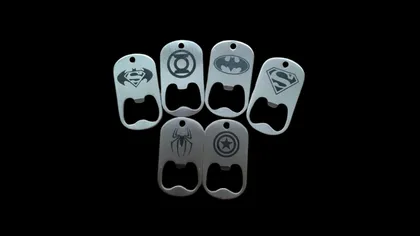 Cinq ouvre-bières en métal avec des logos de super-héros (Superman, Lantern, Batman, Superman, Spider-Man, Captain America) affichés sur un fond noir.