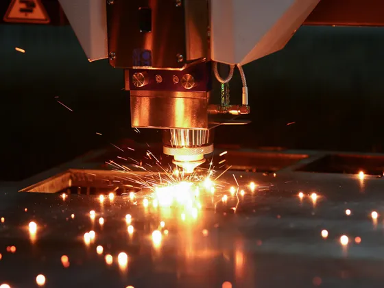 Une machine de découpe laser en action, émettant des étincelles rouges lors de la découpe d'une plaque métallique.