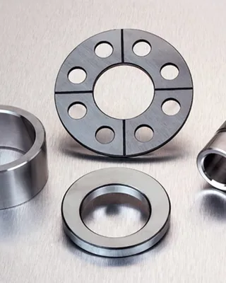Quatre composants métalliques ronds de machines industrielles disposés sur une surface, incluant un roulement à billes, un disque perforé et deux autres pièces cylindriques.