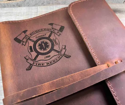 Une pochette en cuir marron avec un logo de la caserne de pompiers, comprenant une étoile de secours et deux haches croisées.