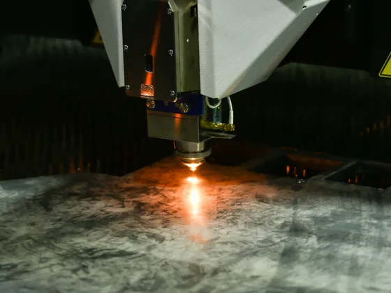Une machine de découpe laser travaillant sur une plaque de métal, avec une lumière orange intense provenant de la zone de coupe.