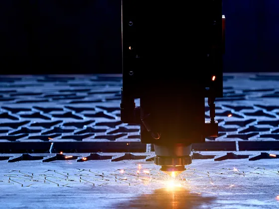 Un robot de soudure laser travaille sur une plaque de métal, produisant des étincelles dans un environnement industriel