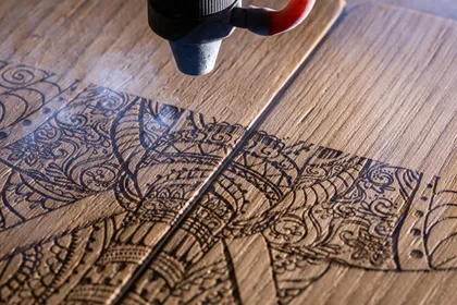 Un laser grave une intricate motif orné sur une planche de bois.