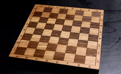 Un échiquier en bois avec un motif de cases claires et foncées, vu en angle sur une surface sombre.