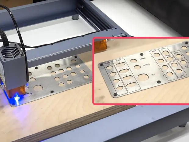 Une machine pour graver ou découper des circuits imprimés avec une plaque en métal percée, une zone d'illuminations bleues, et un panneau de contrôle en dessus, qui est détaché pour l'illustration.