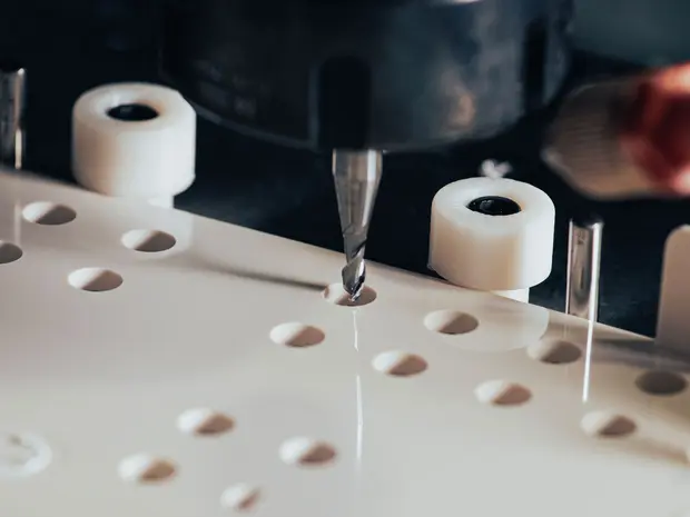 Une machine CNC en train de percer une plaque en plastique blanc. La machine utilise une mèche et est entourée de supports et de rouleaux pour fixer la plaque.