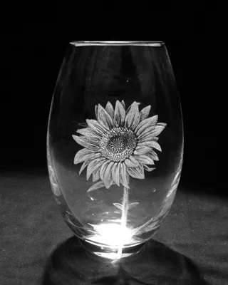Vase en verre transparent avec une peinture d'un tournesol, éclairé par une source de lumière en dessous, sur un fond noir.