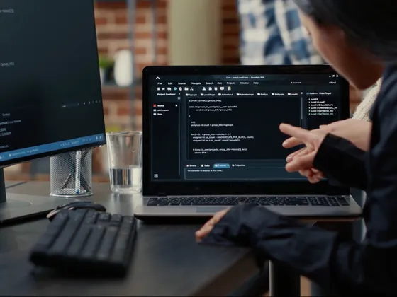 Une personne travaille sur un MacBook avec du code en programmation à l'écran, dans un environnement de bureau.