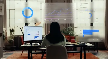 Femme assise à un bureau devant deux écrans d'ordinateur affichant des graphiques et des statistiques de données, avec des graphiques numériques flottants en hologrammes au-dessus de la scène.