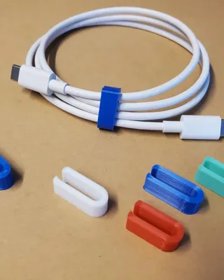 Câble USB blanc avec plusieurs clips de fixation colorés (bleu, blanc, rouge, vert, turquoise) sur une surface beige.