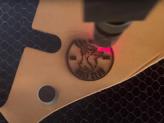 Vue du logo du golf club avec un effet laser ou gravure sur une surface en bois, entourée d'une grille en métal.