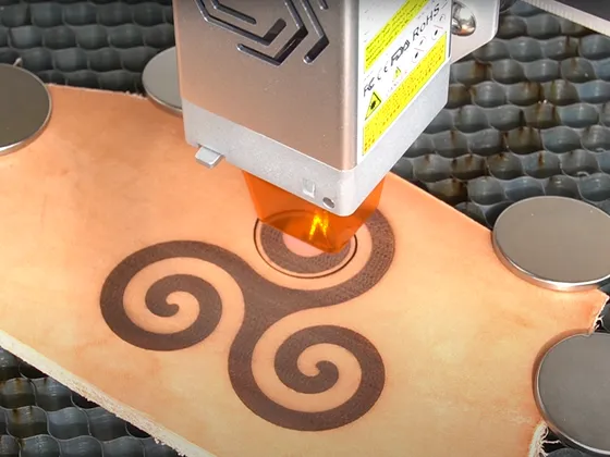 Machine de gravure laser gravant un motif spiralé sur une pièce de cuir orange