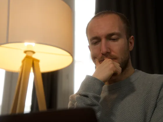 Un homme regarde attentivement un ordinateur portable dans une pièce avec une lampe de lecture à côté.