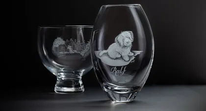Deux verres en verre transparent, un avec une maison et un arbre gravés, l'autre avec un chiot gravé et le nom 'Ralf' gravé en dessous, sur un fond noir.