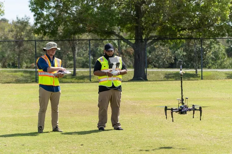 Deux personnes en gilets de sécurité pilotant un drone de surveillance dans un parc
