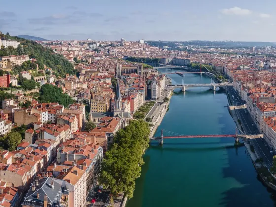 Vue aérienne de la ville de Lyon, France, montrant la Saône avec plusieurs ponts, des bâtiments anciens, et la basilique Notre-Dame de Fourvière sur la colline à gauche.