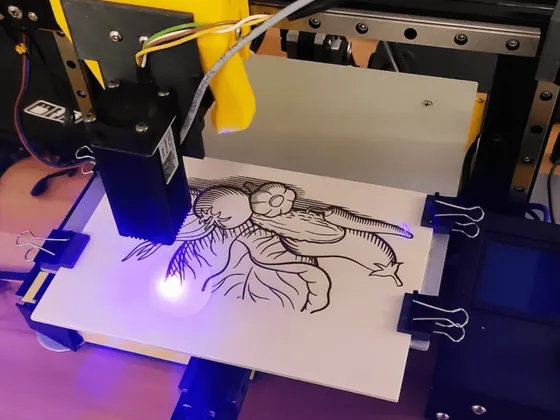 Une imprimante 3D en action imprimant une illustration détaillée d'une plante avec un visage, utilisant une lumière bleue UV pour révéler l'encre sur une planche en bois.