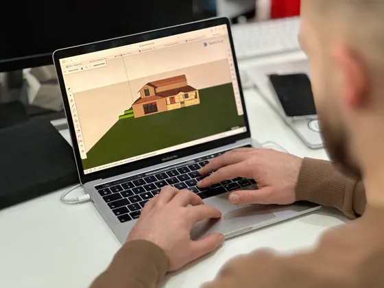 Person travaillant sur un ordinateur portable, affichant un modèle 3D d'une maison sur l'écran.