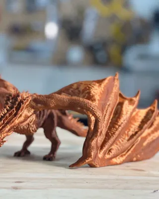 Modèle réduit de dragon en métal cuivreaux, avec ailes déployées, placé sur une surface en bois.