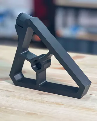 Pièce en plastique noir en forme de triangle avec une ouverture centrale, posée sur une surface en bois, en milieu d'atelier.
