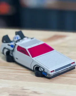 Modèle réduit d'une voiture de sport, blanc avec une calandre grise, avec une vitre avant rouge, posé sur une surface en bois.
