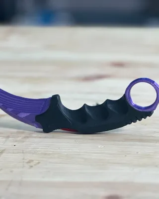 Une dague de combat en plastique noir, avec une lame en vert foncé et une garde en violet et noir, posée sur une table en bois.