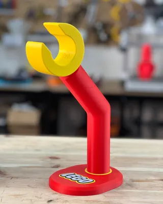 Un support à level LEGO rouge avec une pince jaune en haut, placé sur une surface en bois.
