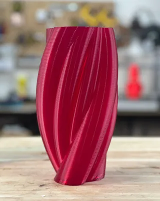 Vase rouge en verre avec motifs torsadés, posé sur une surface en bois.