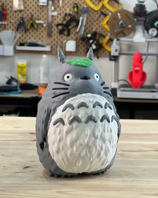 Figurine en argile ou en pâte à modeler représentant Totoro, un personnage de film d'animation, avec une tête grise, un ventre blanc avec des motifs en forme de 'V' et un peu de pâte verte sur la tête.