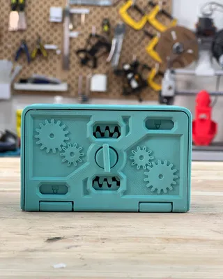 Un boîtier en plastique bleu contenant des engrenages et des pièces mécaniques, placé sur une table en bois avec un mur d'outils en arrière-plan.