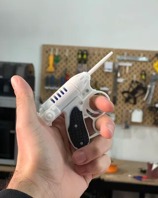 Une personne tient une sculpture en forme de pistolet dans un atelier, avec des outils accrochés à un panneau de liège en arrière-plan.