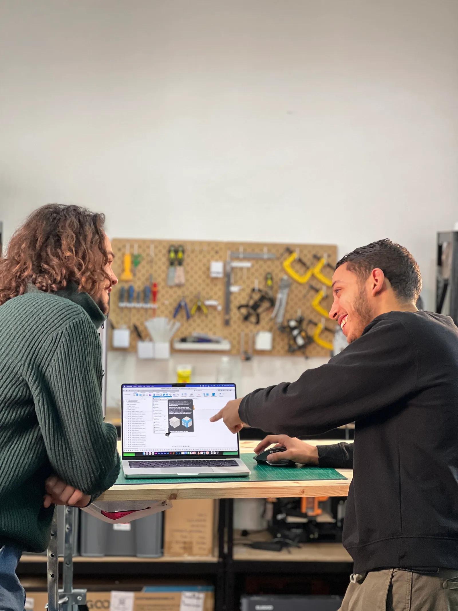 Deux hommes discutent dans un atelier devant un ordinateur portant des modèles 3D