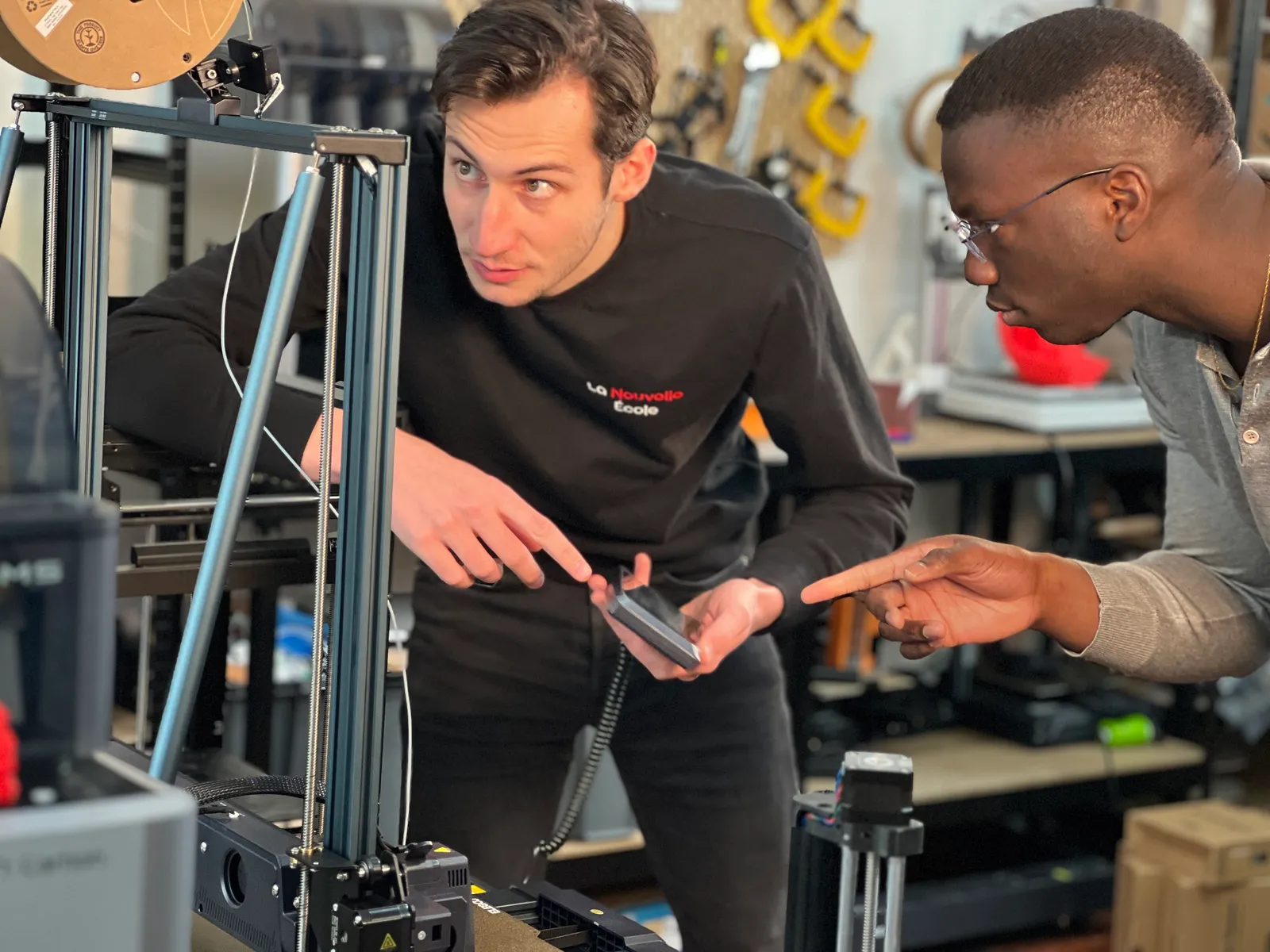 Deux hommes discutent devant une imprimante 3D dans un atelier technique