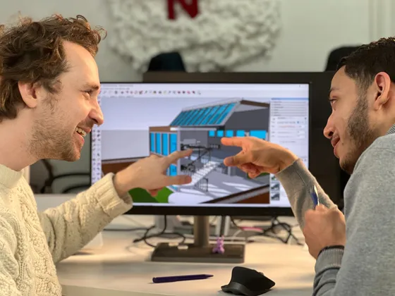 Deux hommes discutent et pointent vers un écran d'ordinateur affichant un modèle 3D d'une maison moderne