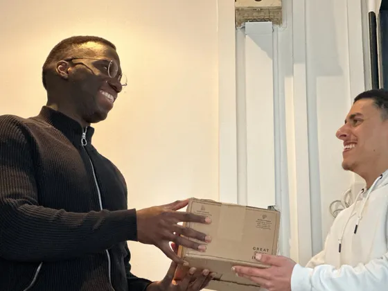 Une personne souriante remet une boîte à une autre personne souriante qui se tient dans une petite fenêtre.
