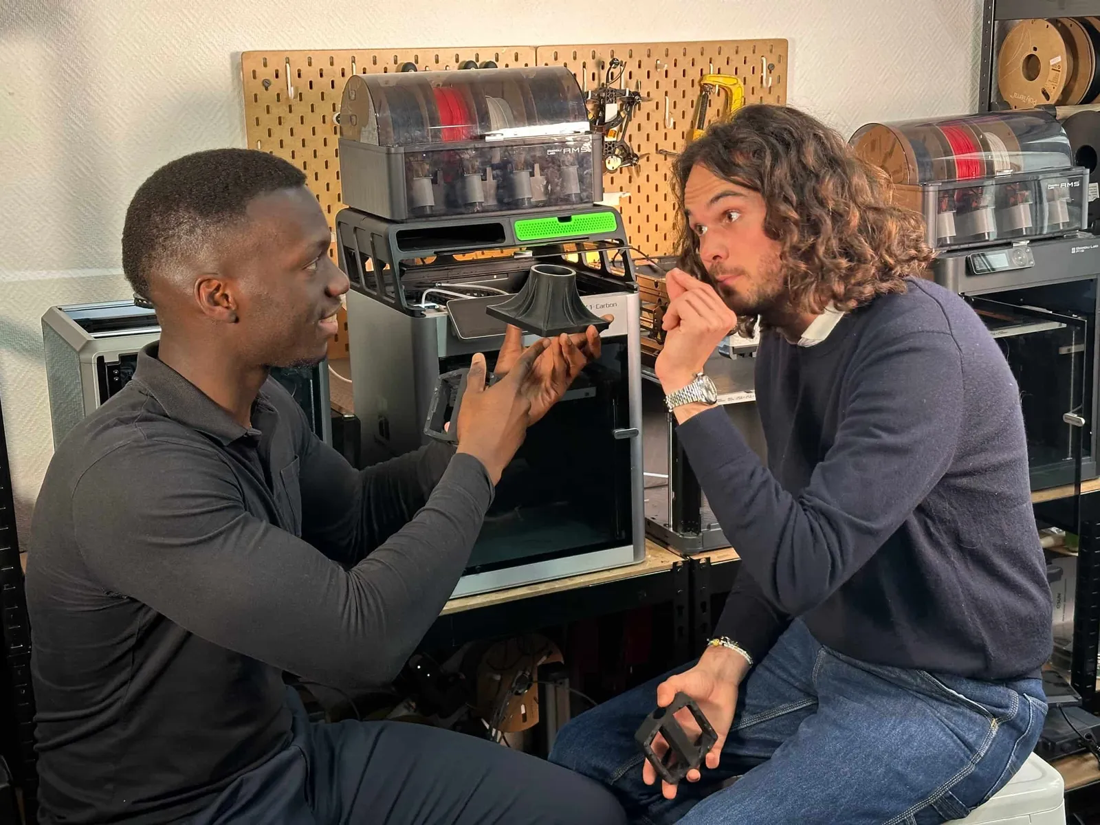 Deux jeunes hommes discutent dans un atelier, l'un montre une pièce imprimée à l'autre