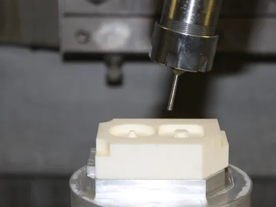 Un dispositif industriel avec un outil en cours de fabrication ou de modification, situé au-dessus d'une pièce en plastique ou en résine sur une table ou une machine.