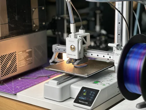 Une imprimante 3D en action, utilisant un filament coloré pour imprimer un objet sur une plateforme de construction, dans un environnement de laboratoire ou atelier.