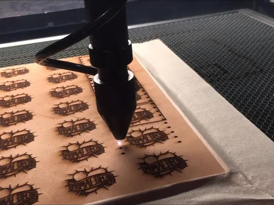 Une machine de gravure laser est en train de graver un logo sur une planche de bois. Le logo représente un soleil avec des rayons autour et un texte en dessous.