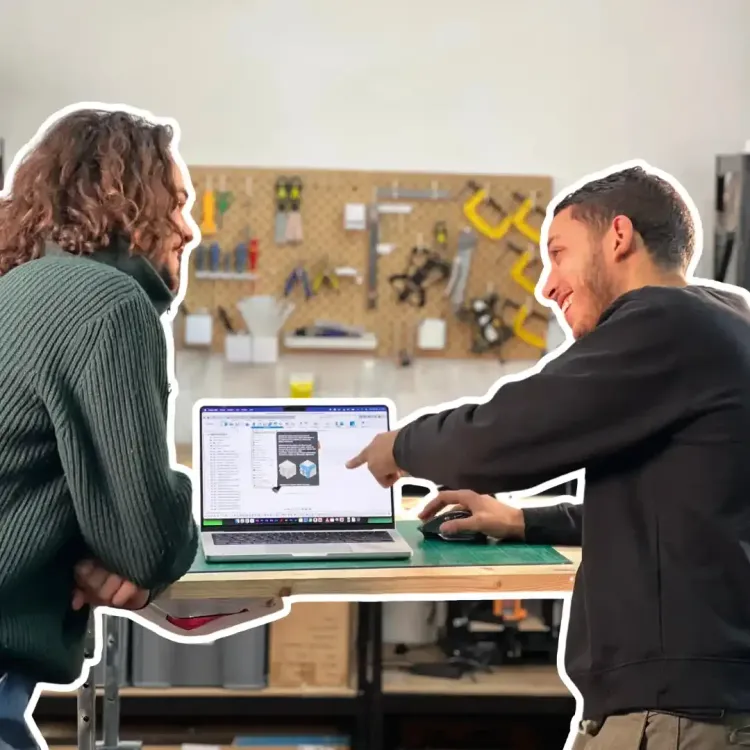 Deux personnes échangent devant un ordinateur portable dans un atelier