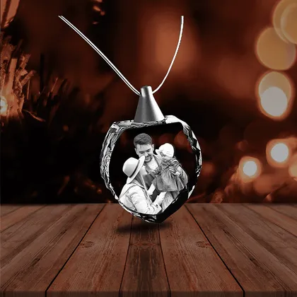 Une boule de Noël en forme de cœur contenant une photo en noir et blanc de deux adultes et d'une enfant souriant.