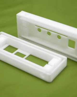 Deux boîtiers en plastique blanc, probablement pour des appareils électroniques, posés sur une surface verte.