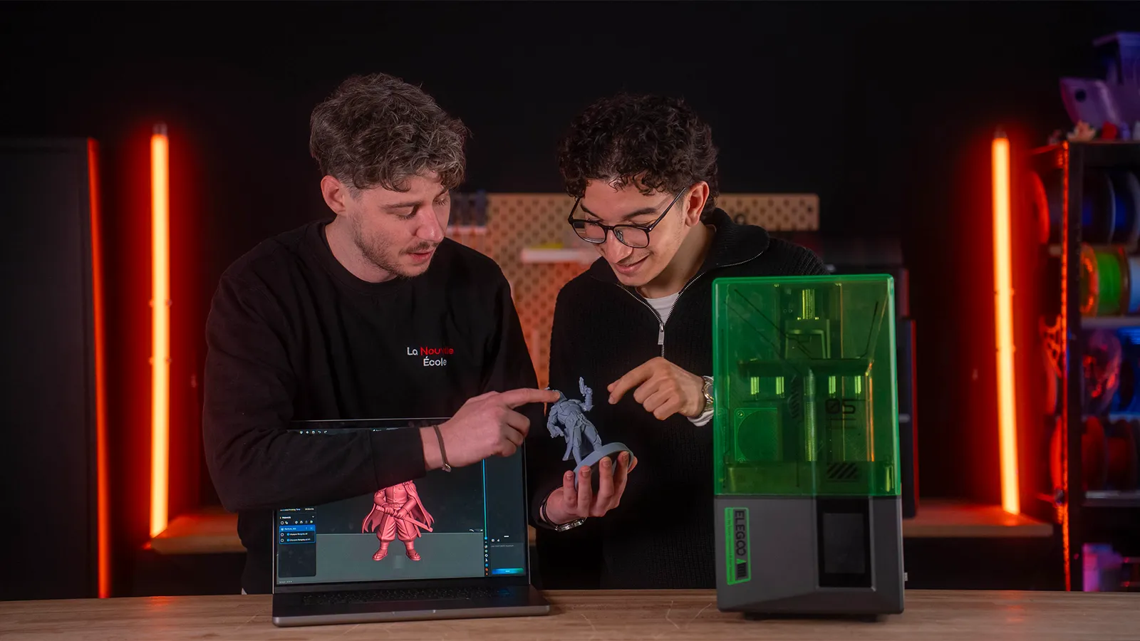 Deux formateurs de La Nouvelle École présentent une figurine imprimée en résine, devant l\'imprimante et le modèle 3D