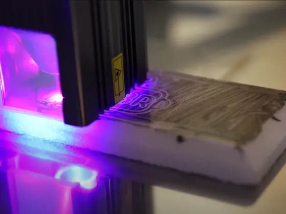 Une imprimante 3D utilisant une lumière violette pour imprimer sur une surface en bois avec une couche blanche de support