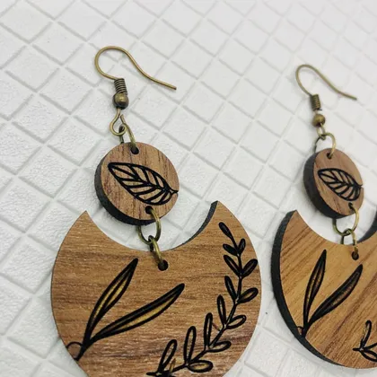 Boucles d'oreilles en bois avec motif de feuilles noirs.