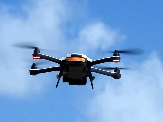 Un drone en vol dans un ciel bleu avec quelques nuages.